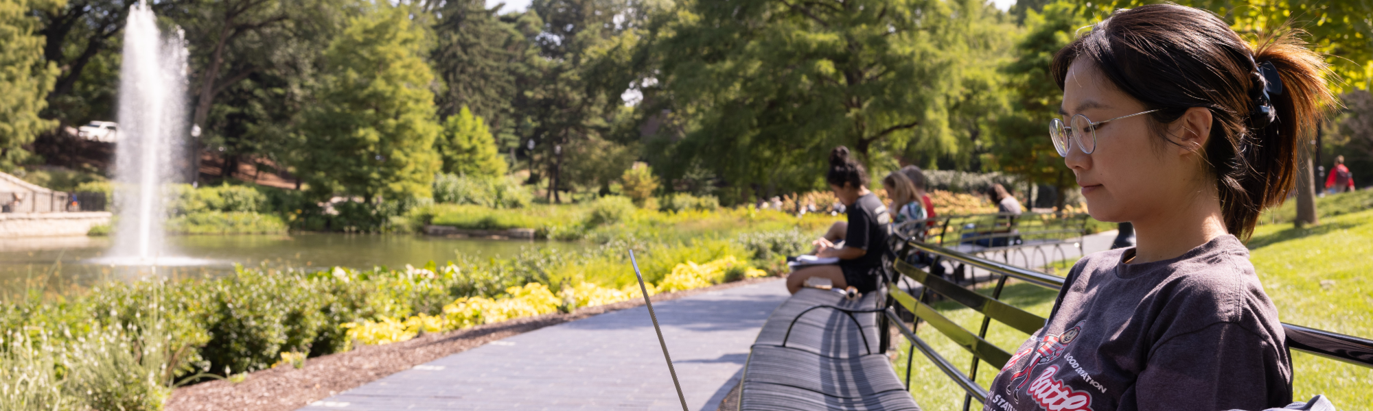 A person sitting on a park bench using a laptop and mirror lake in the background