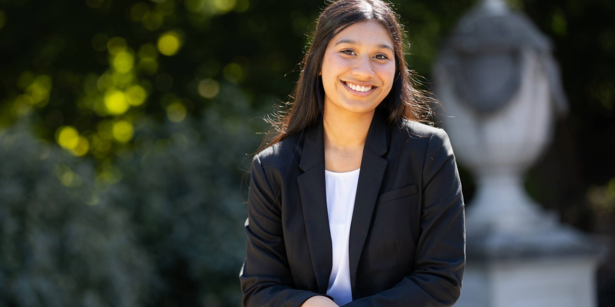 Individual smiles in professional clothing with greenery and statue in the background