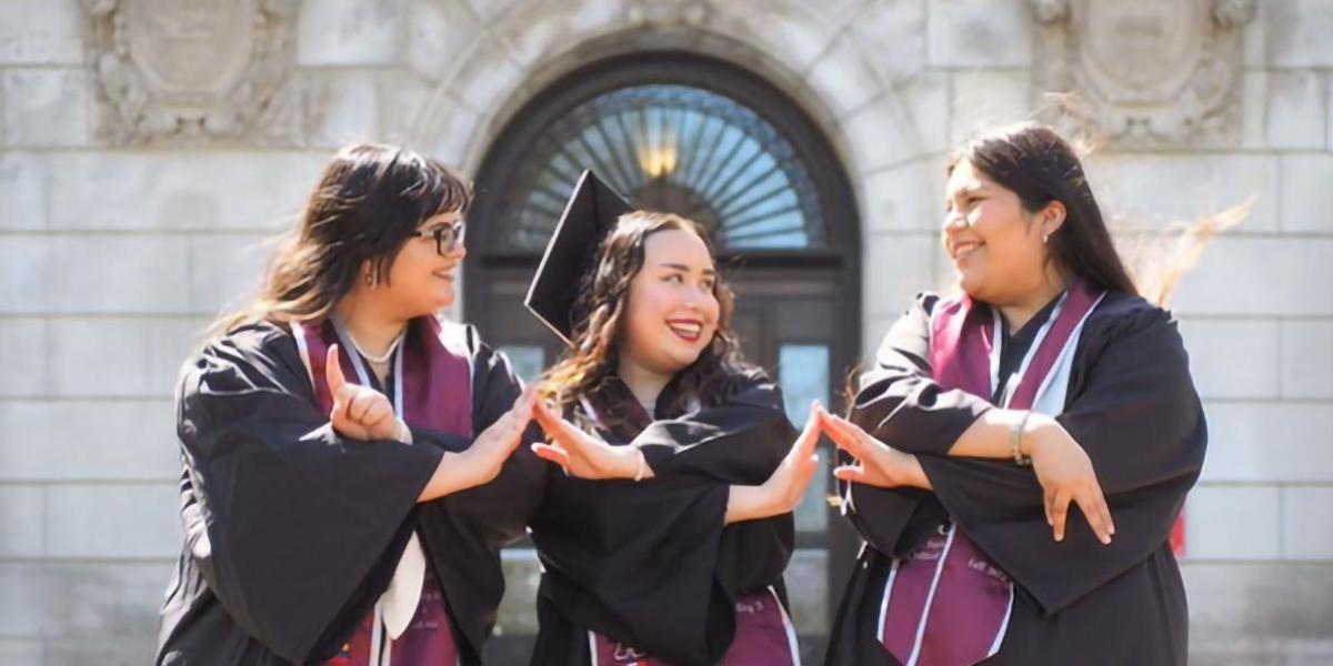 Regina Loayza, dressed in a cap and gown, touches hands with fellow graduates and friends.