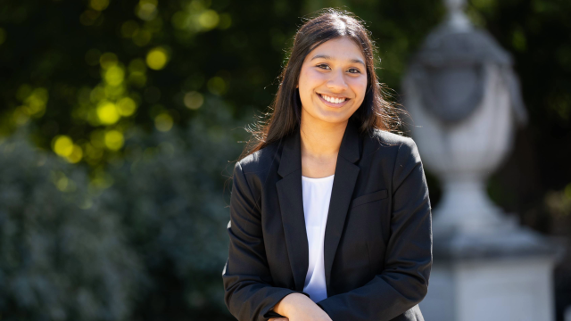 Individual smiles in professional clothing with greenery and statue in the background