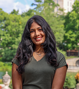Divya smiles in an outdoor setting of lush greenery.