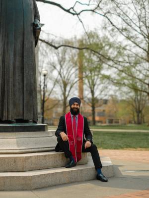 Anitvir S. Taunque in formal attire and a red graduation stole sits on the steps of the Thompson statue at The Ohio State University
